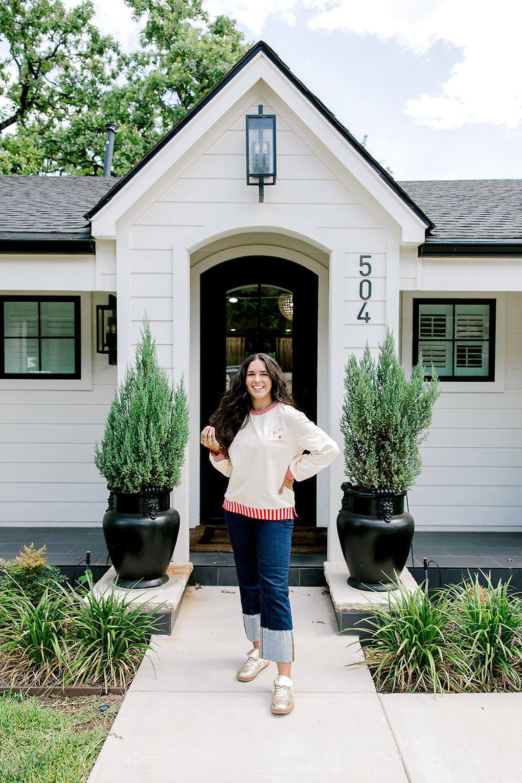 Woman with dark hair wearing a sweatshirt with red & white striping along cuff and collar. On the back of top there is a multi color bible verse. Model paired this top with dark-wash denim jeans. 