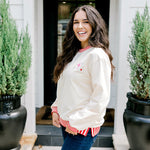 Woman with dark hair wearing a sweatshirt with red & white striping along cuff and collar. On the back of top there is a multi color bible verse. Model paired this top with dark-wash denim jeans. 
