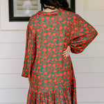 Woman with dark hair wearing a red/green otomi graphic dress that is long-sleeve & has slight ruffle at bottom of dress.
