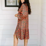 Woman with dark hair wearing a red/green otomi graphic dress that is long-sleeve & has slight ruffle at bottom of dress.