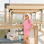 Woman with blonde hair standing in a side profile position wearing the Molly Top and Kate Shorts in a lifestyle scene. The focal point of this image is the outfit in it's entirety as well as seeing it in "real time". The model has this paired with multi-color sneakers. 
