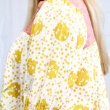 Woman with blonde hair in deep focal perception with a focus on the tops shoulder graphics. This image is against a white background. 