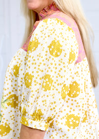 Woman with blonde hair in deep focal perception with a focus on the tops shoulder graphics. This image is against a white background. 