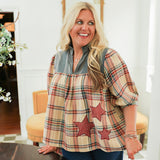 Woman with blonde hair wearing a quarter sleeve top with plaid patch-work paired with dark-wash denim jeans. 