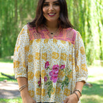 Woman with dark hair in front facing position wearing the TInley Top while against a background with heavy greenery. She has this top paired with light-wash denim jeans.