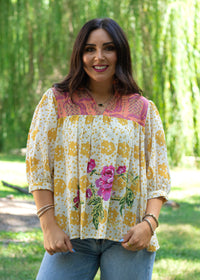 Woman with dark hair in front facing position wearing the TInley Top while against a background with heavy greenery. She has this top paired with light-wash denim jeans.