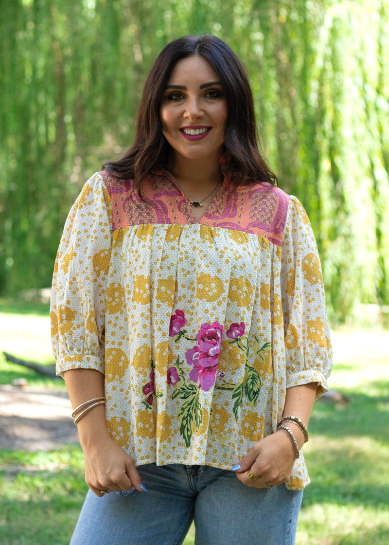 Woman with dark hair in front facing position wearing the TInley Top while against a background with heavy greenery. She has this top paired with light-wash denim jeans.