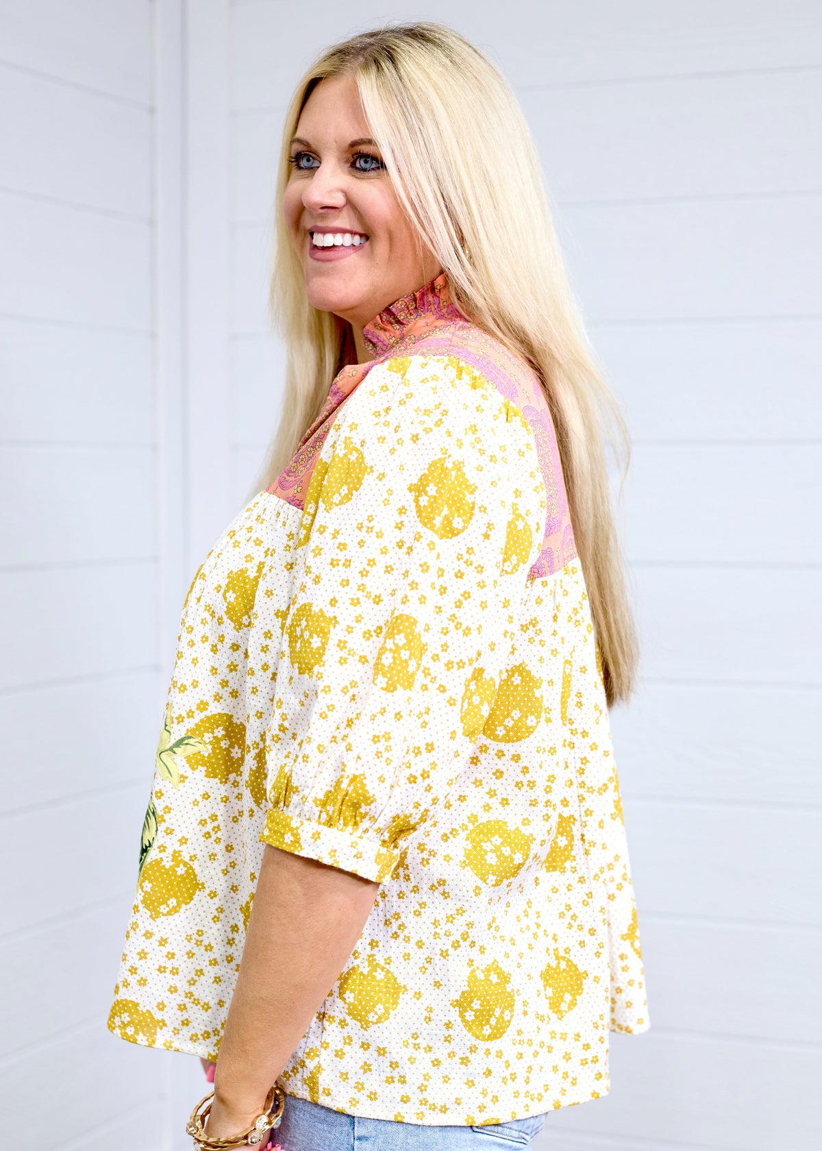 Woman with blonde hair in a side profile position showing the side graphics of the Tinley Top. She has this top paired with light-wash denim and is against a white background. 