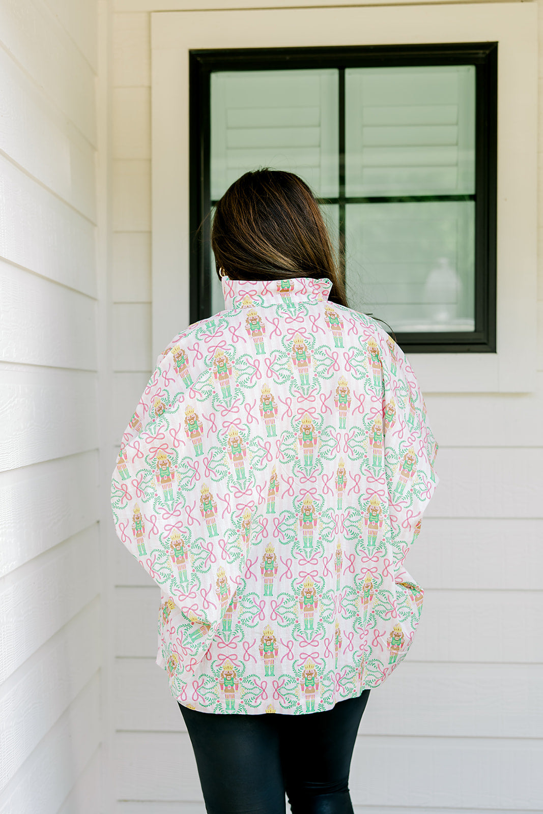 Woman with dark hair wearing a top in the Tori body style featuring pink & green nutcracker graphics. Model paired this top with faux leather leggings.
