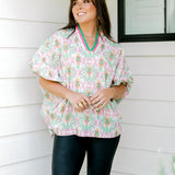 Woman with dark hair wearing a top in the Tori body style featuring pink & green nutcracker graphics. Model paired this top with faux leather leggings.