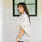 Woman with dark hair wearing a top in the Tori body style featuring pink & green nutcracker graphics. Model paired this top with faux leather leggings.