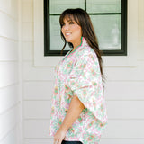 Woman with dark hair wearing a top in the Tori body style featuring pink & green nutcracker graphics. Model paired this top with faux leather leggings.