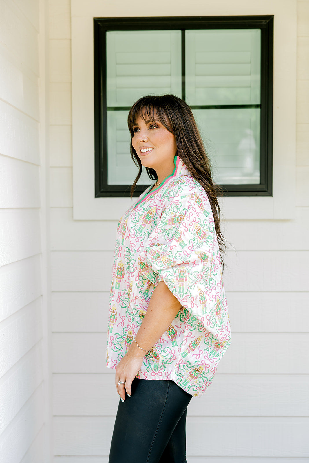 Woman with dark hair wearing a top in the Tori body style featuring pink & green nutcracker graphics. Model paired this top with faux leather leggings.