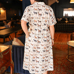 Woman with dark hair wearing a short-sleeve midi dress with multi-colored horses and belt to tie around wait. 