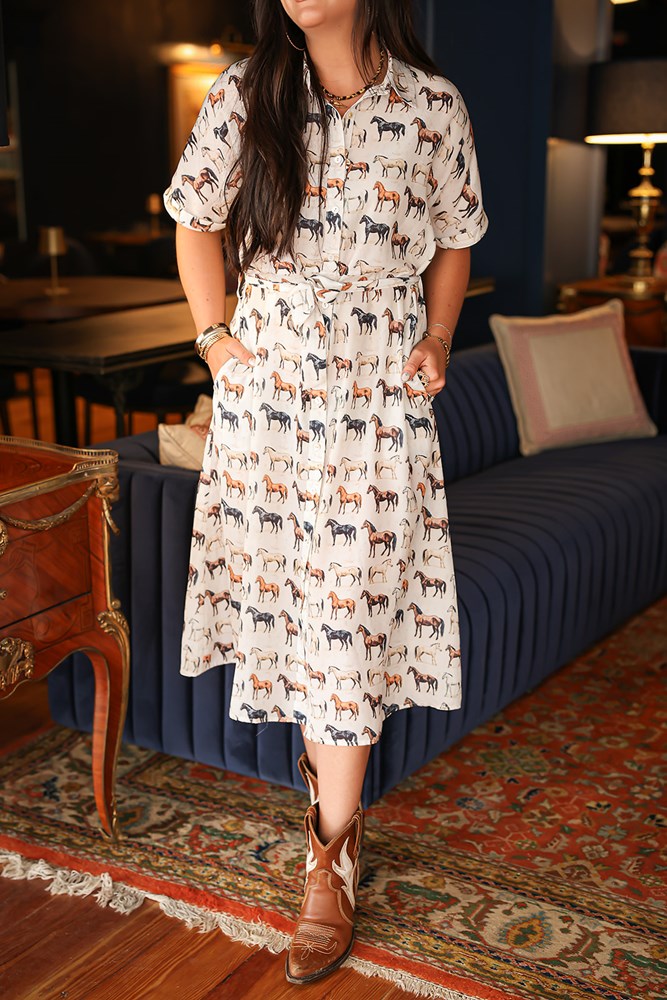 Woman with dark hair wearing a short-sleeve midi dress with multi-colored horses and belt to tie around wait. 
