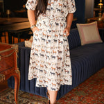 Woman with dark hair wearing a short-sleeve midi dress with multi-colored horses and belt to tie around wait. 