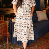 Woman with dark hair wearing a short-sleeve midi dress with multi-colored horses and belt to tie around wait. 
