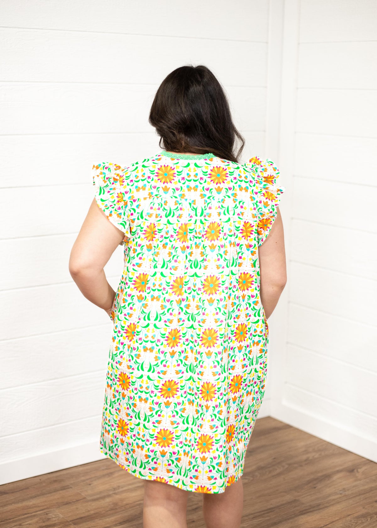 Woman with dark hair standing in a back profile position wearing the Wren Dress against a white background. The focal point of this image is to show the graphic on the back of the dress as well as show the length of the dress. 