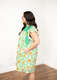 Woman with dark hair standing in a side profile position wearing the Wren Dress against a white background. The focal point of this image is the embroidery on the side of the dress as well as ruffled sleeves. 